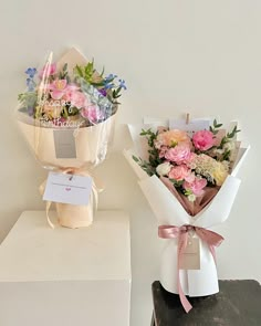 two bouquets of flowers sitting on top of a white box next to each other