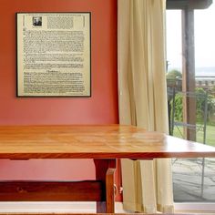 a wooden table sitting in front of a window next to a wall with a poem on it