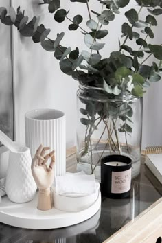 a vase filled with green leaves next to a candle and other items on a table