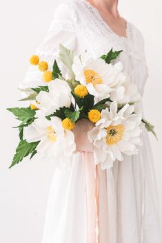 a woman holding a bouquet of white and yellow flowers in her hands, wearing a white dress