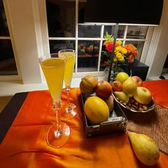 two glasses of orange juice and some fruit on a table