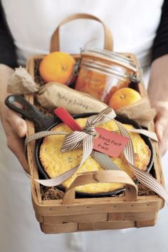 a person holding a basket filled with bread and oranges next to some jam jars