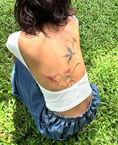 a woman sitting in the grass with her back turned to the camera and tattoos on her body