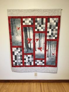 a red and black quilt hanging on the wall next to a wooden floor in front of a white wall