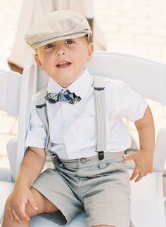 a little boy sitting on top of a white chair wearing a bow tie and suspenders