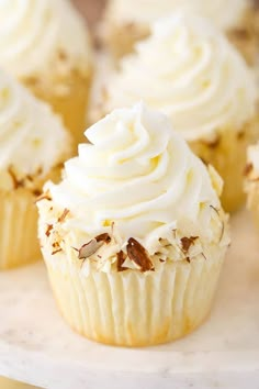 cupcakes with white frosting and sprinkles sitting on a table