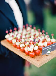 a wooden tray topped with small appetizers on top of a green grass covered field