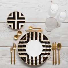 a black and white table setting with gold cutlery, plates, cups and utensils