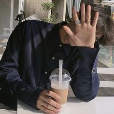 a man holding his hand up in the air while sitting at a table with a drink