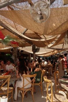 people sitting at tables under an umbrella covered area with chairs and tablecloths on it