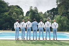 a group of men standing in front of a pool wearing blue pants and white shirts