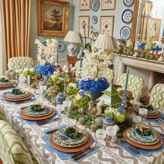 a dining room table is set with blue and white flowers, candles, plates and vases