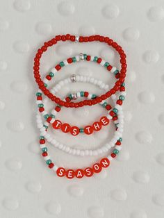 three red and white beaded bracelets with the words tis the season written on them