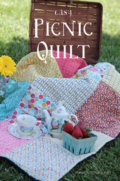 a picnic quilt with strawberries and tea on the grass next to a basket full of flowers