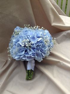 a bridal bouquet with blue flowers and baby's breath on the bed sheet