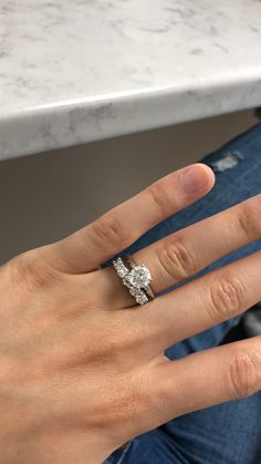 a woman's hand with a diamond ring on top of her left hand, sitting at a marble countertop