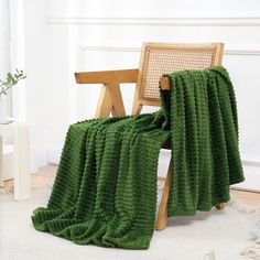 a green blanket sitting on top of a wooden chair next to a white rug in a room