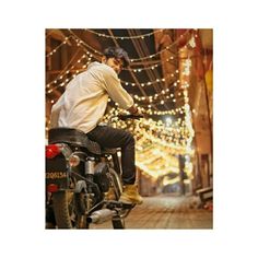 a man riding on the back of a motorcycle down a street covered in christmas lights