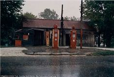 three old fashioned gas pumps in front of a run down building on a rainy day