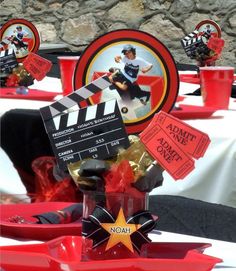 a table topped with red plates and cups filled with movie themed items, including a clapa board