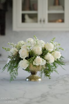 a vase filled with white flowers sitting on top of a marble countertop next to cabinets