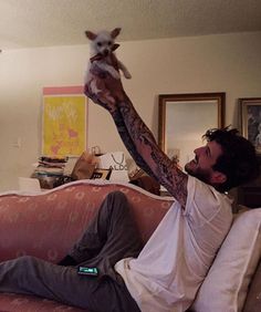 a man sitting on top of a couch holding up a small dog