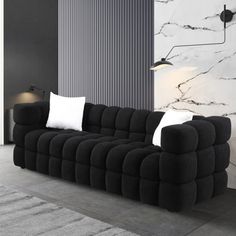 a living room with black couches and white pillows on the floor in front of a marble wall