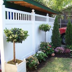 a red truck parked next to a white fence in a yard with flowers and trees