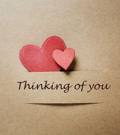 two paper hearts with the words thinking of you written on them, placed in front of a piece of cardboard