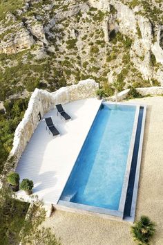 an empty swimming pool in the middle of a rocky area with two lounge chairs next to it