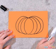 someone is drawing a pumpkin on an orange piece of paper