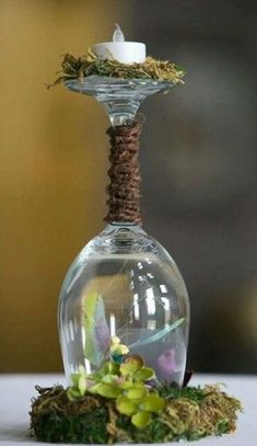 a small glass vase with moss and a candle on the top is sitting on a table