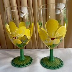 two wine glasses with yellow flowers painted on the bottom and green rims, sitting side by side