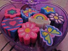 a purple heart shaped container filled with lots of different types of candles and decorations on top of a table