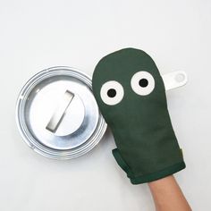 a hand with a green mitt on it next to a metal can and an object