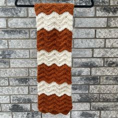 a brown and white crocheted scarf hanging on a brick wall next to a black hook