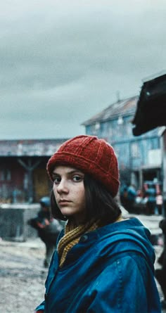 a woman in a red hat and blue coat is standing on the street with other people