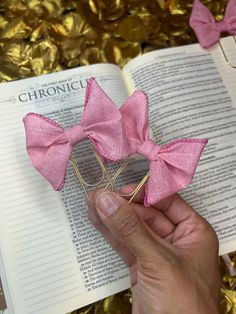 a hand holding a pink bow on top of an open book next to gold foil