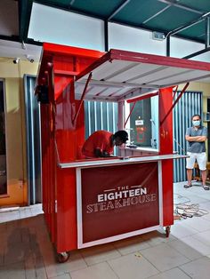 a man standing in front of a red and white food cart with the words eighteen steakhouse on it