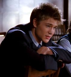 two young men sitting next to each other in front of a wooden table and chairs