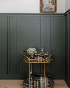 a bar cart with drinks on it in front of a painting and green paneled walls