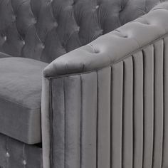 a grey velvet couch with pleated back and tufted cushions on the armrests