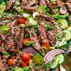 steak salad with tomatoes, cucumbers and onions in a black bowl on a wooden table