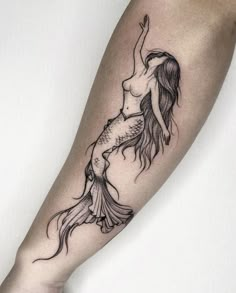 a black and white photo of a mermaid tattoo on the right arm, with her tail in the air