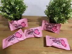 five pink candy bags sitting on top of a wooden table next to potted plants