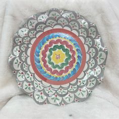 a decorative plate is sitting on a white blanket and it looks like an ornament