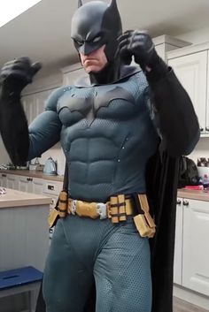 a man dressed as batman standing in a kitchen