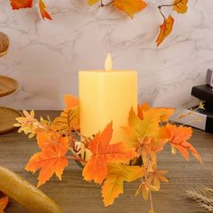 a lit candle sitting on top of a wooden table next to autumn leaves and bread