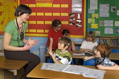 there are many children sitting at desks and one woman is talking to the other