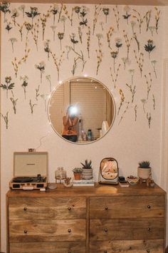 a dresser with a mirror on top of it next to a wallpapered flower pattern